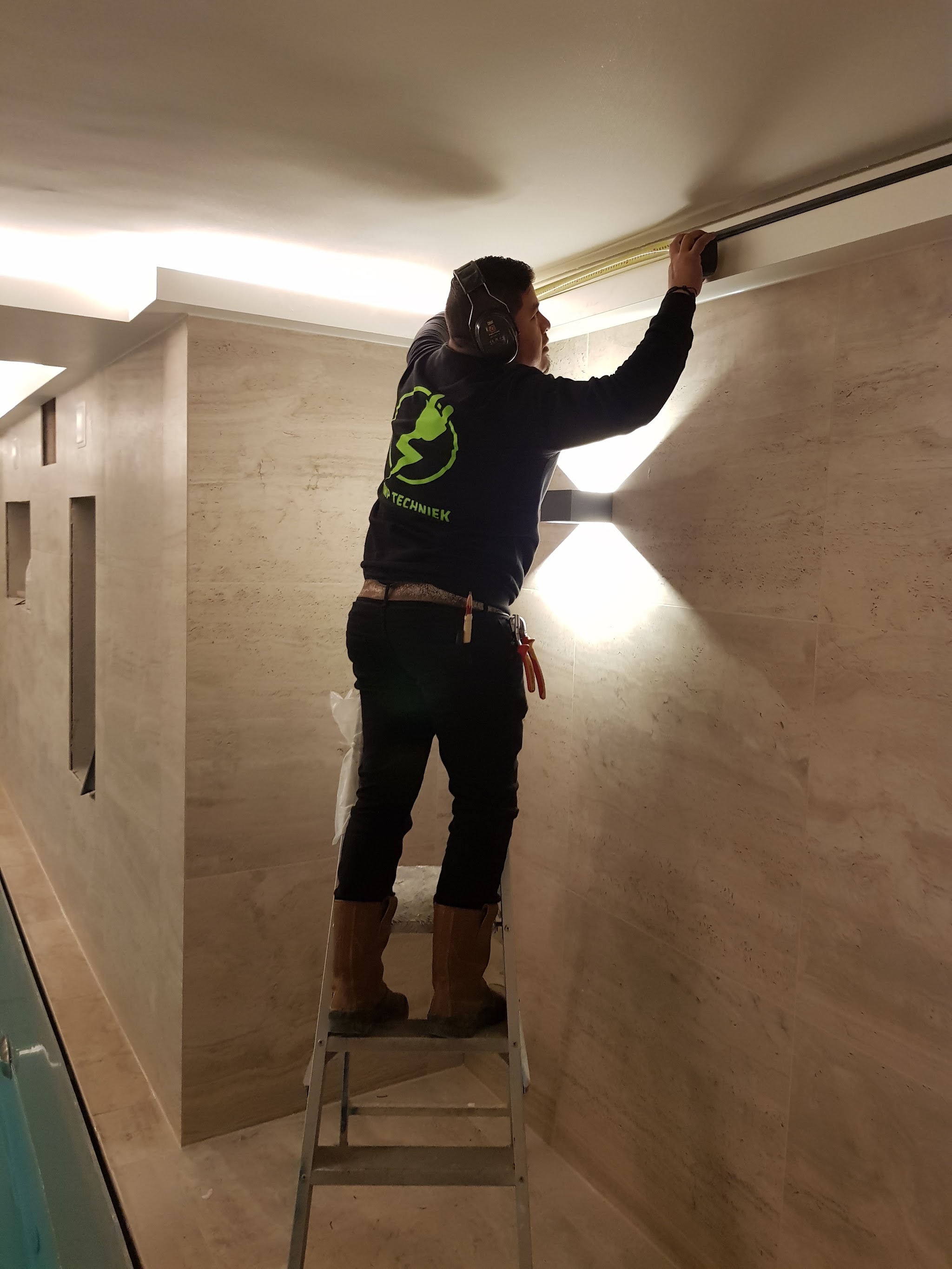 Roberto van RMP Elektrotechniek monteert een LED-strip boven een betegelde wand
